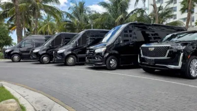 Professional chauffeur in a dark suit holding a car door open for a guest outside a Coral Gables estate