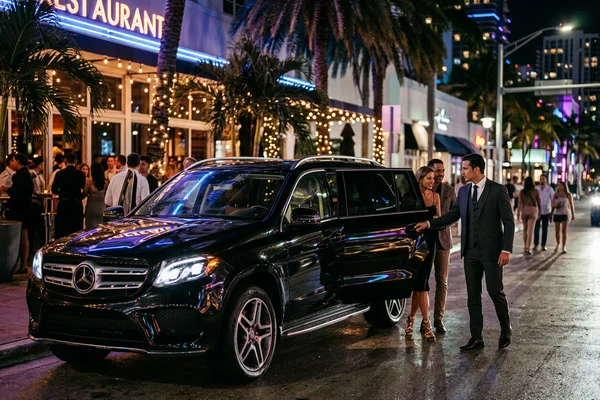 Black luxury vehicle arriving at an upscale Miami nightlife venue at night with chauffeur service