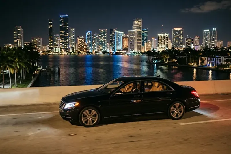 Group of friends in evening attire laughing and toasting champagne inside the illuminated cabin of a luxury limousine with Miami city lights visible through tinted windows