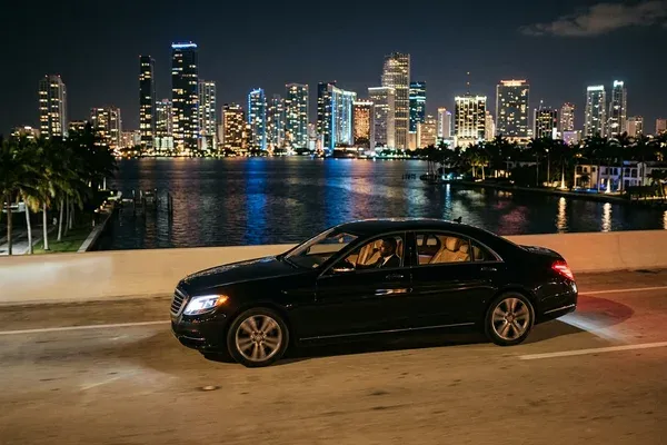 Executive reviewing a tablet in the rear of a luxury sedan approaching Brickell Avenue office towers during morning commute with the Miami skyline visible