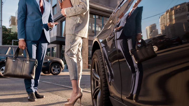 Cropped photo of two business people in classic wear standing near black car outdoors.
