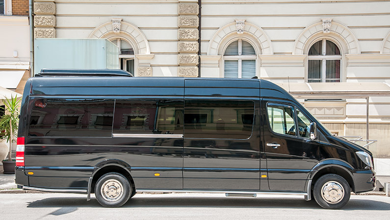 Mercedes Benz sprinter black luxury shuttle bus van parked on the street.
