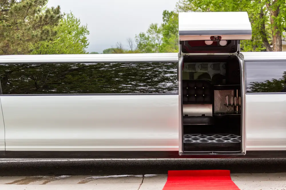 White luxury limousine with open up door and red carpet leading to. 
