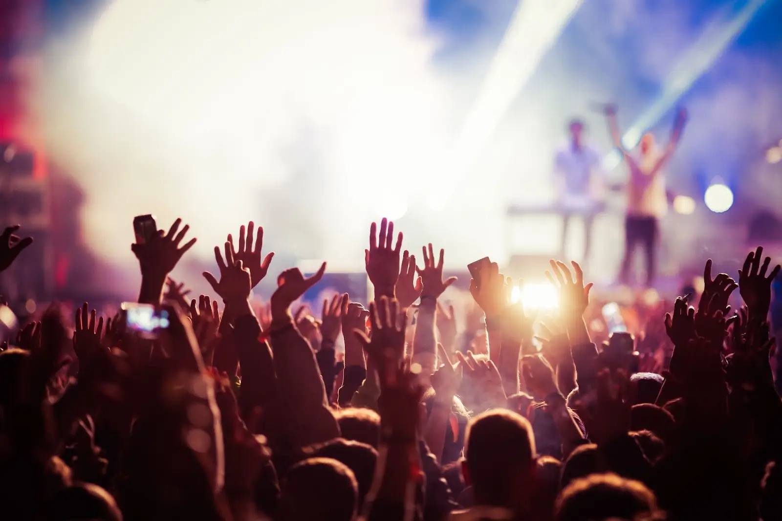 people at concert with hands in the air and stage in background