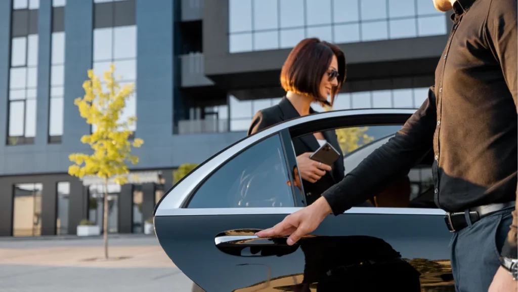 A professional chauffeur opens the car door for a woman, showcasing premium car service in Miami with attention to detail.