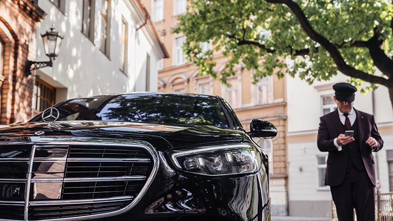 Riga, Latvia 21 July 2021 Limousine transfer chauffeur with chauffeur hat, stands by luxury car. Holding Mobile phone in hand. Mercedes Benz S500 S class w223
