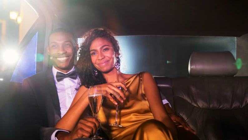 Smiling celebrity couple drinking champagne inside limousine outside event