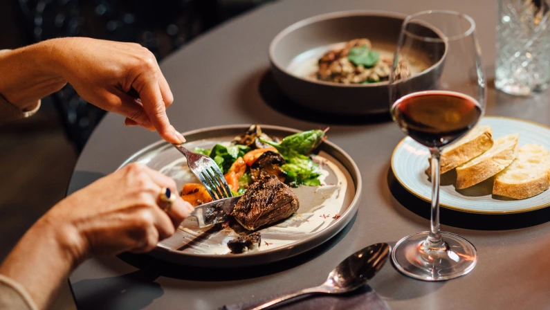 Elegant restaurant dining scene featuring ostrich fillet with grilled vegetables, fresh salad, and red wine, captured in a sophisticated, modern setting.