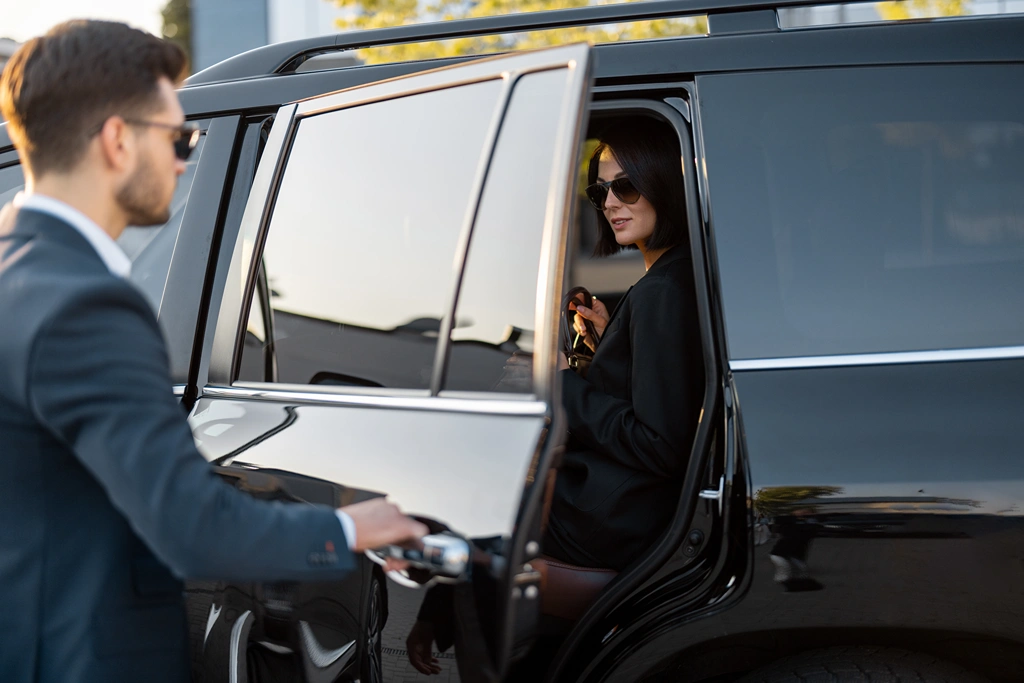 Business man helps business lady to get in the car, opening vehicle door. Concept of business trip and travel
