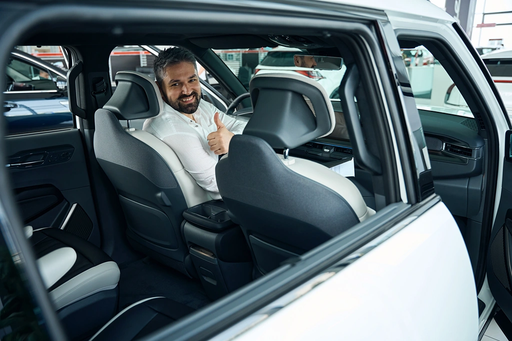Happy man checking new luxury car, showing thumbs up in dealership center