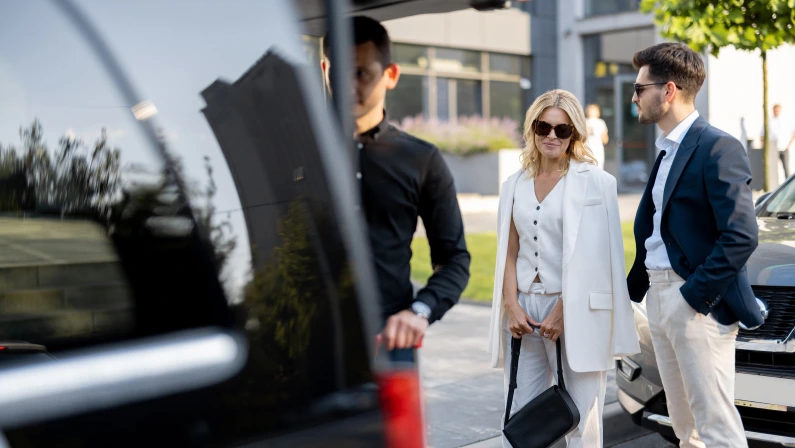 Business couple standing by a minivan taxi waiting for their chauffeur or porter to help them with a suitcases. Concept of business trips and travel