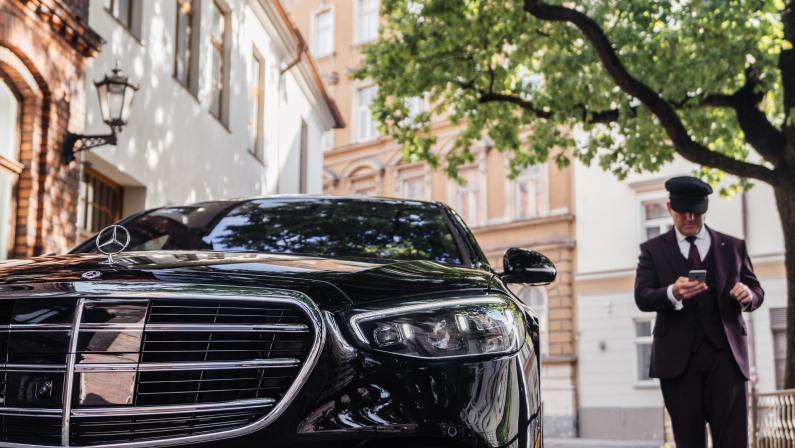 Riga, Latvia 21 July 2021 Limousine transfer chauffeur with chauffeur hat, stands by luxury car. Holding Mobile phone in hand. Mercedes Benz S500 S class w223